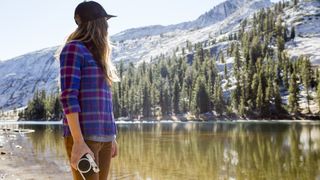 A woman holding a Polaroid camera while hiking next to a lake in Yosemite