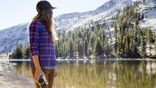 A woman holding a camera while hiking next to a lake in Yosemite