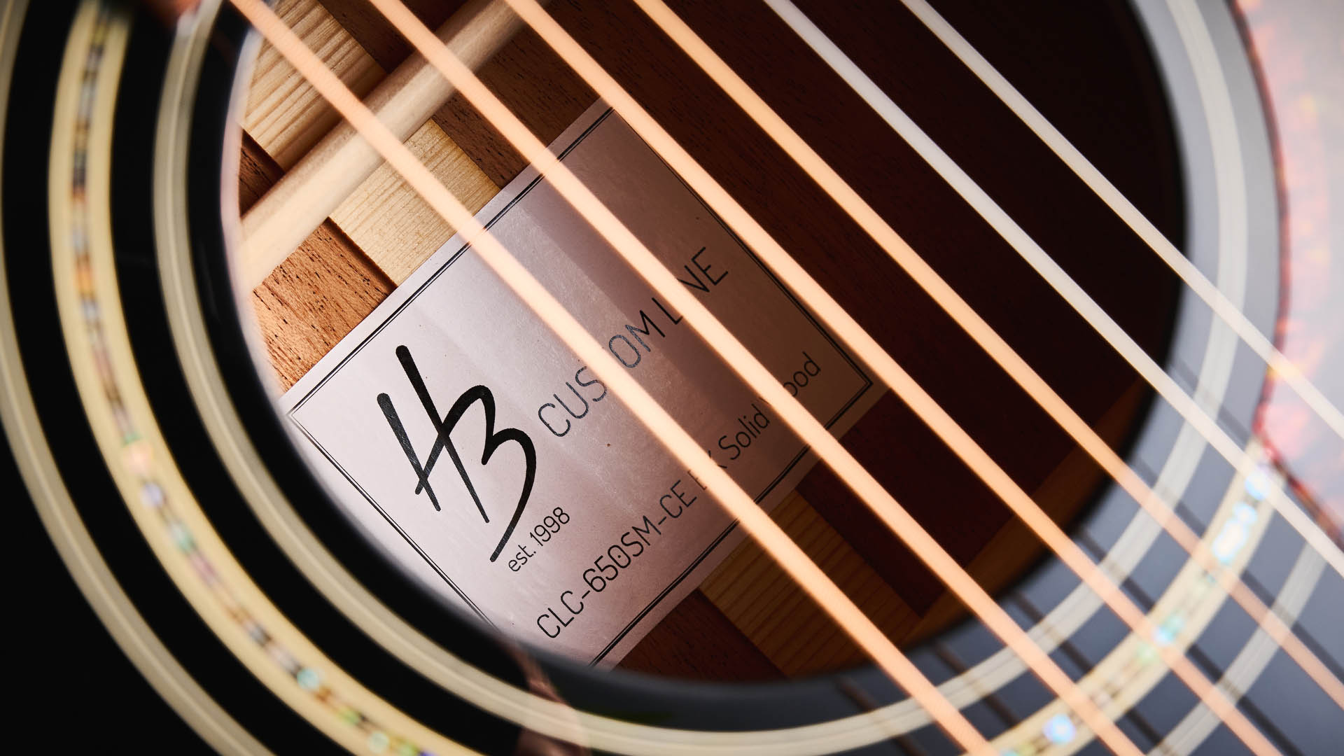 Harley Benton CLC-650SM-CE: the affordable cutaway electro-acoustic has a black top, natural back and sides, with an attractive arm-rest and tortoiseshell pickguard, and is here photographed against a wooden floor.