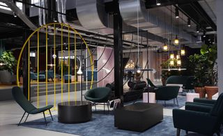 The Student Hotel lobby with yellow metal divider, dark teal armchairs, pot plants in terracotta pots and blue rugs