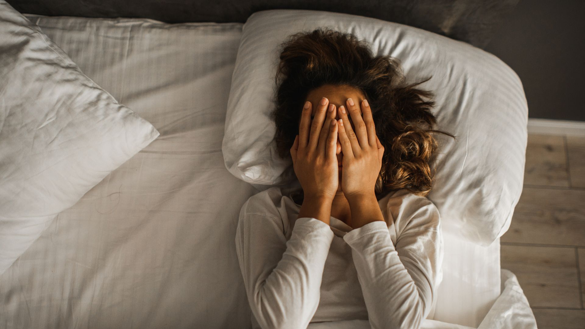 Woman lying in bed covering her face