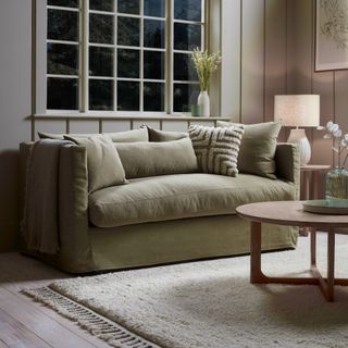 Cox & Cox Colmar two-seater sofa in green in an evening-time living room with a switched on table lamp and a round coffee table