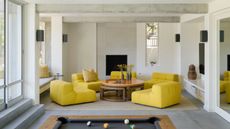 living room with white walls, concrete surfaces, four bright yellow armchairs arranged around a round timber coffee table and a pool table in the foreground