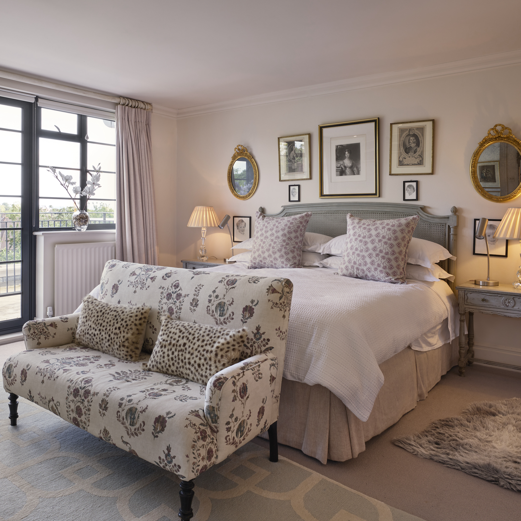 bedroom with grey french style bed with two seater sofa at base and pictures on the wall above headboard