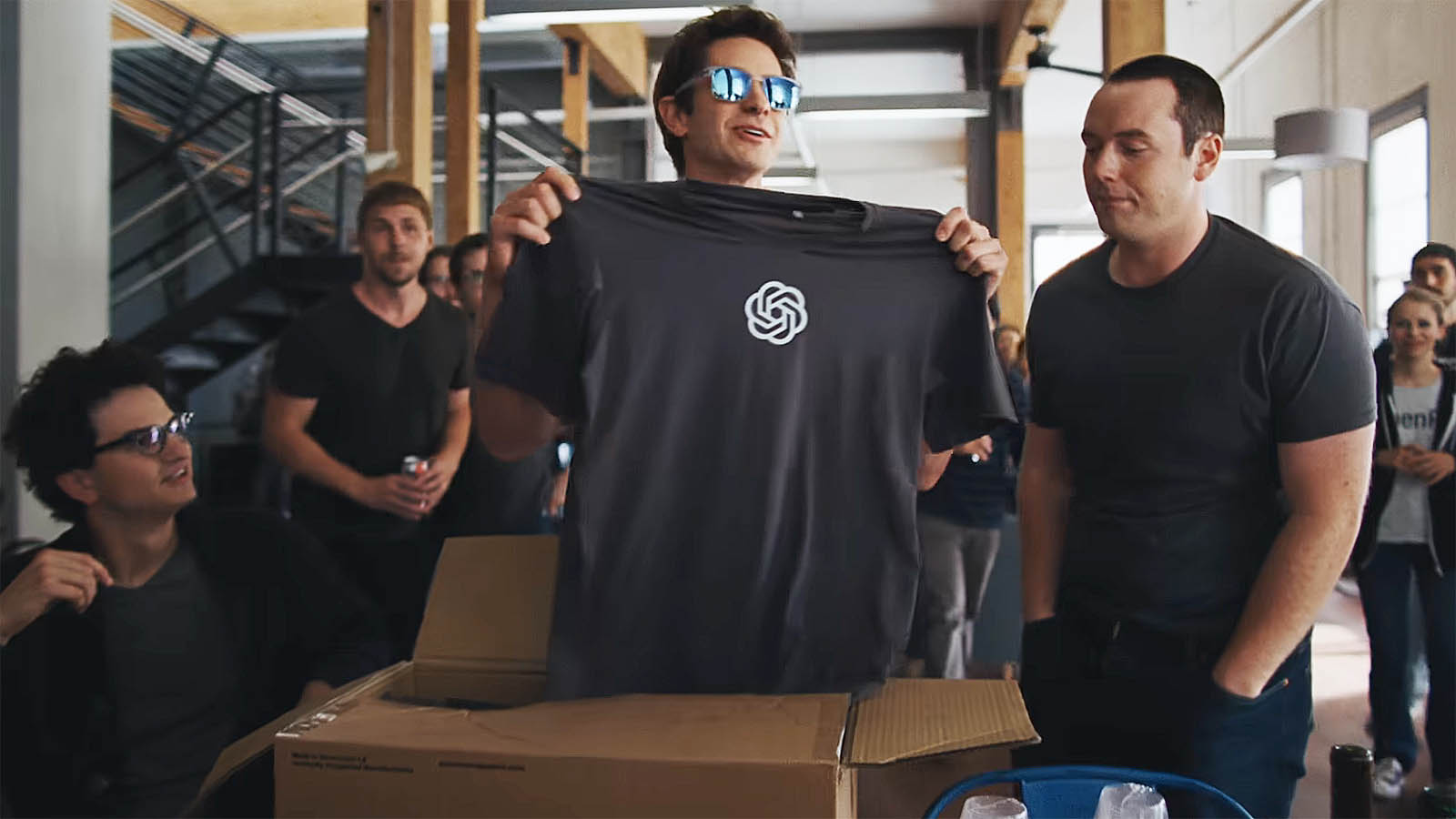 Andrew Garfield's Sam Altman holding up a T-shirt with the ChatGPT logo on it in Neon's Artificial movie