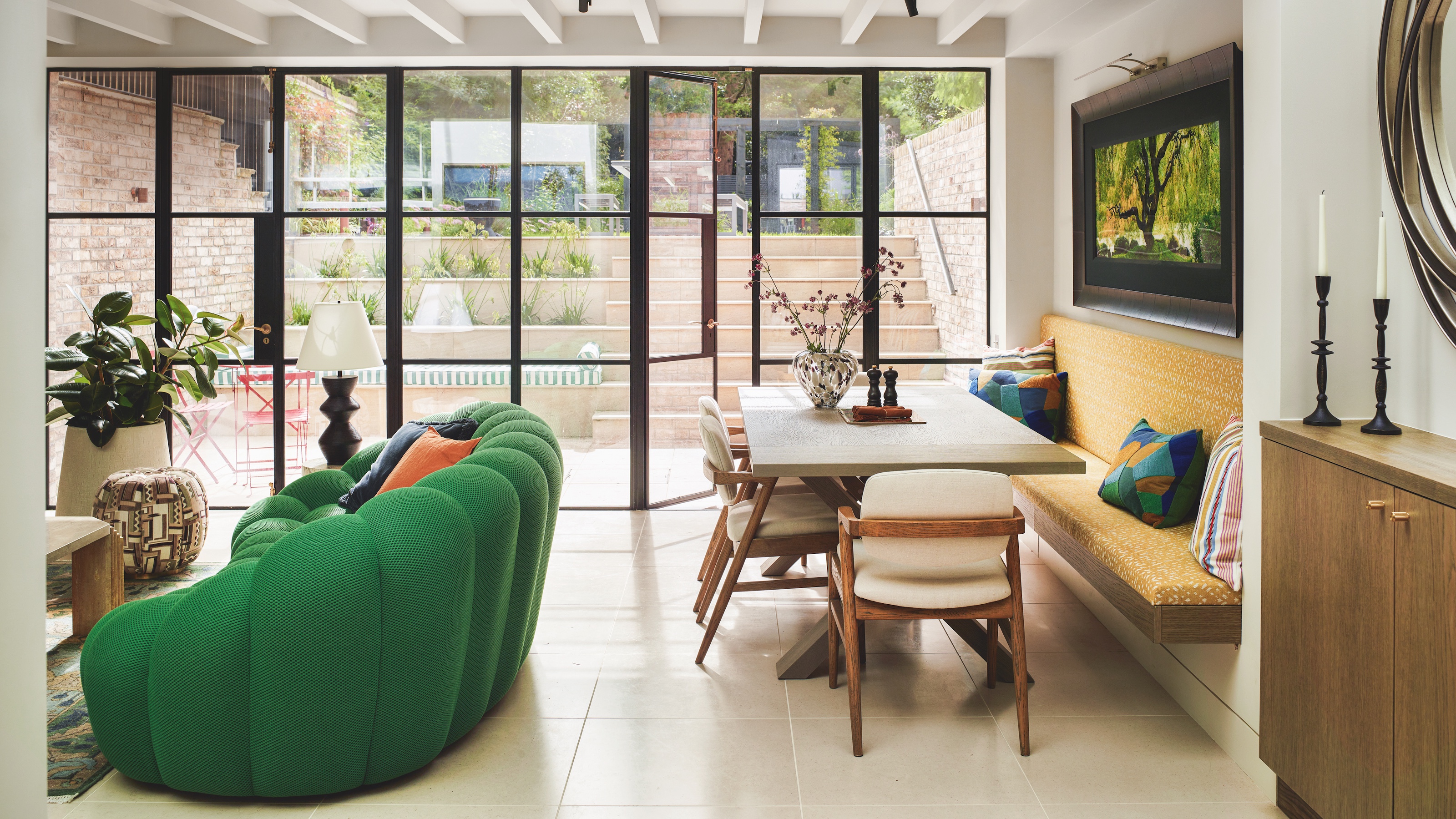 open plan kitchen living space with green sofa and wooden dining table with crittall sytle doors to courtyard garden