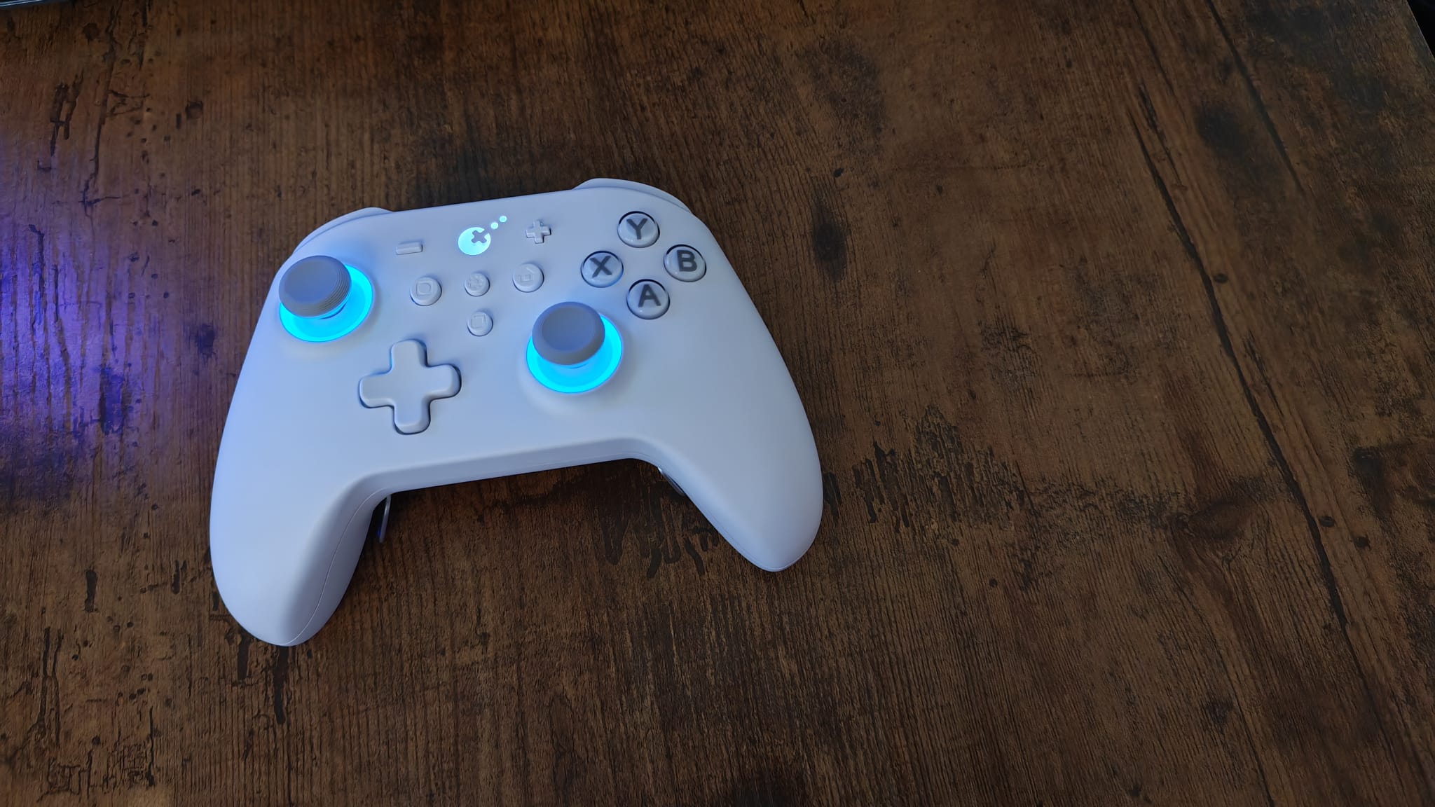 A white Gulikit KK3 Max controller on the left of the picture, lying on a walnut desk surface