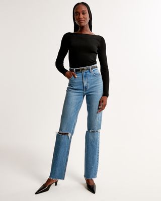 Abercrombie & Fitch model in black top and high waisted blue ripped jeans