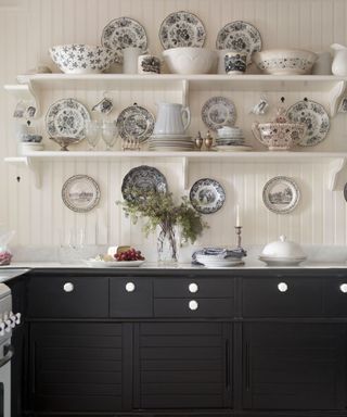 black kitchen cabinets with white wood panelled walls, shelves with eclectic farmhouse decor and crockery