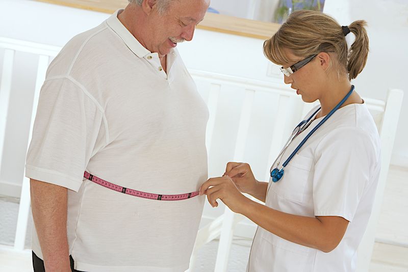 A doctor measures the waistline of one of her overweight patients.