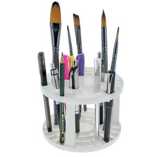 A white circular paintbrush holder filled with pens and paintbrushes