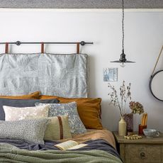 Bed with hanging headboard, piles of pillows on bed and dried flowers on bedside table