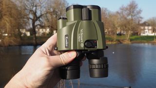 Kenko VC Smart Cellarto 10x30 WP binoculars held in a hand outside in front of a lake