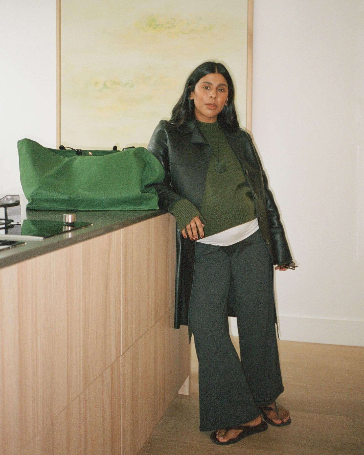 Monikh Dale wearing a green leather car coat with a matching sweater and drawstring pants.
