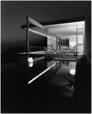 Chuey House, black and white night time image, narrow swimming pool, reflecting the night lights, patio area with seating leading into the house, balcony to the left side, with view of surrounding landscape