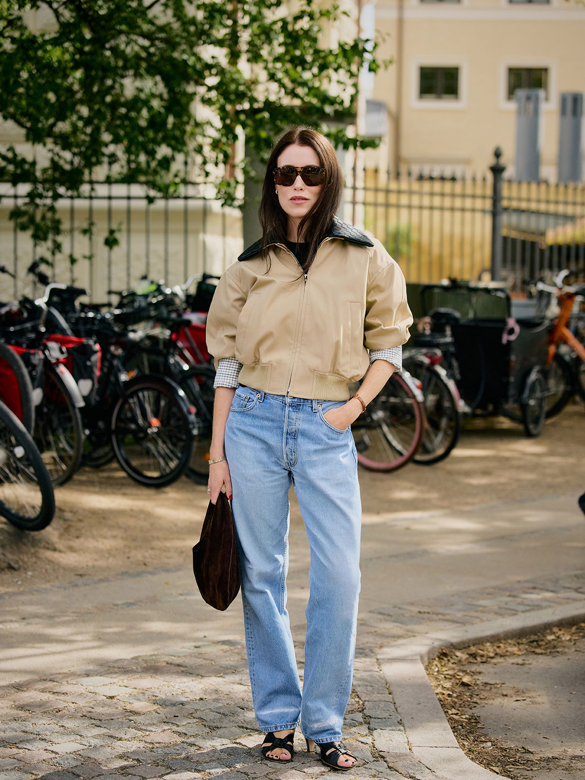 Woman wearing a tan blouson and light-wash jeans.