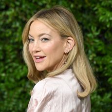 a white woman with short, blonde hair posing at a red carpet event in front of a flower wall