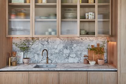 a close up of a wood and marble kitchen with reeded glass cabinet uppers