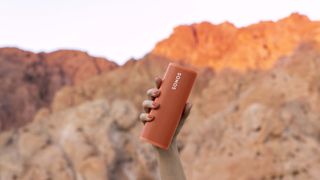 Sonos Roam orange speaker being held up in the desert at sunset