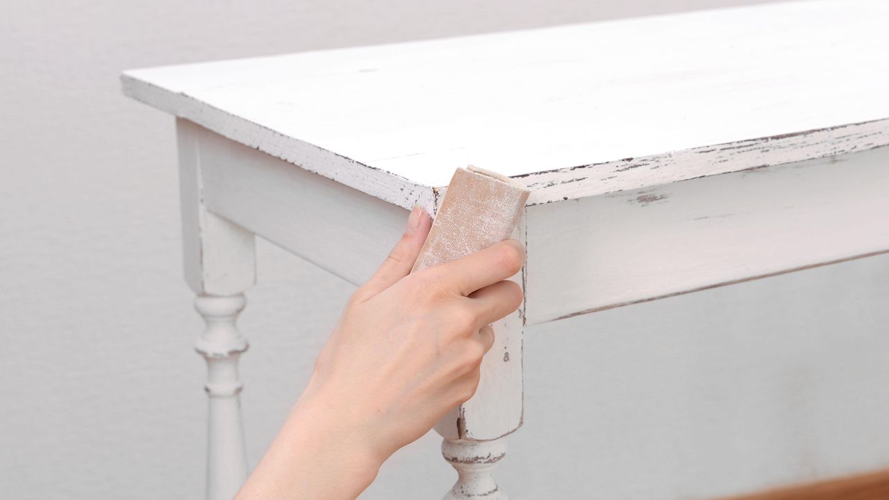 Female hand removing paint from wooden table for decoration, indoors