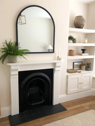 Arched mirror hanging above newly installed fireplace and pinewood surroundings
