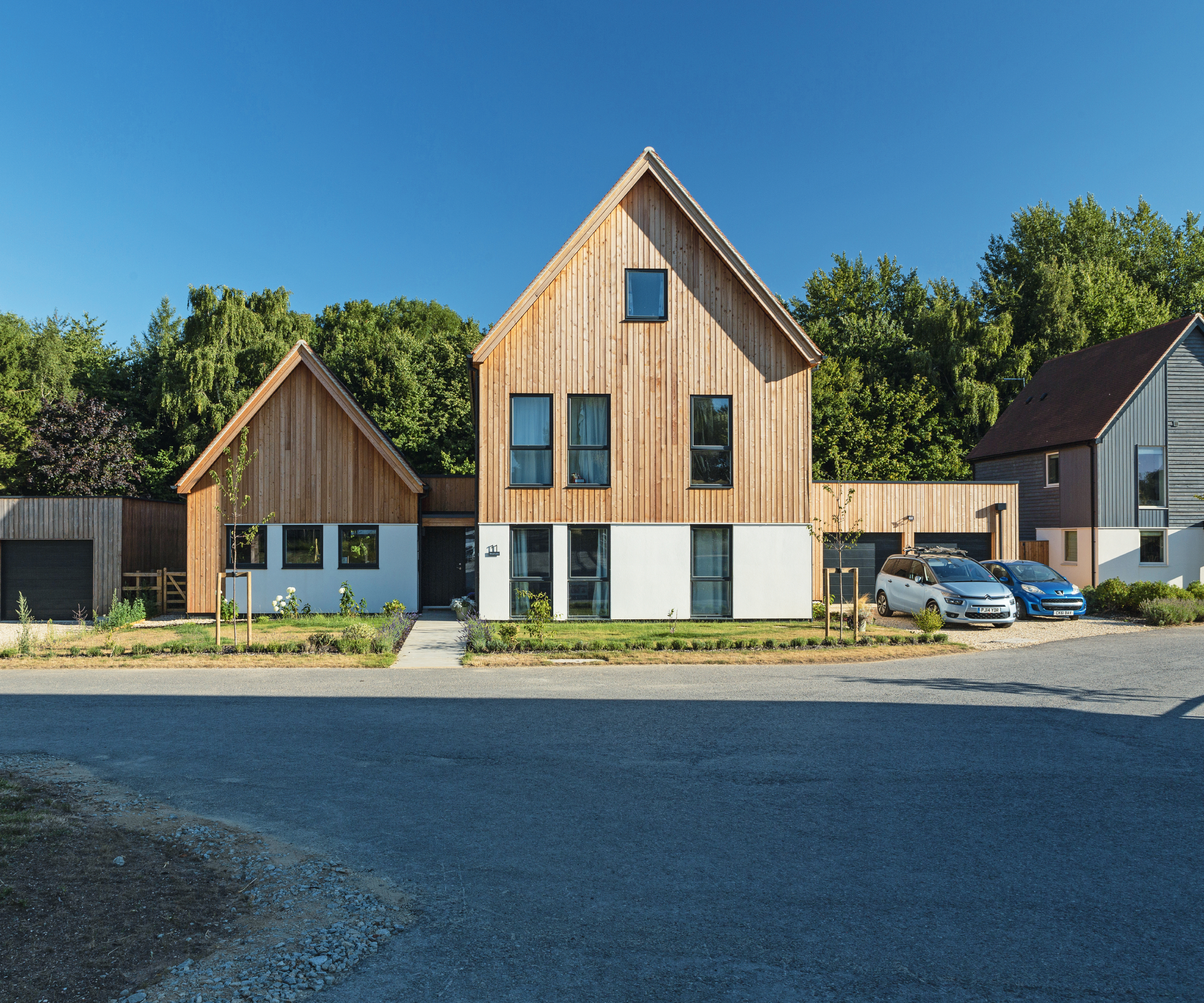 modern white rendered and wooden clad house with driveway leading straight onto road