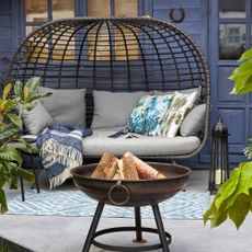 A garden with a curved rattan garden sofa with a firepit and an outdoor floor lamp 