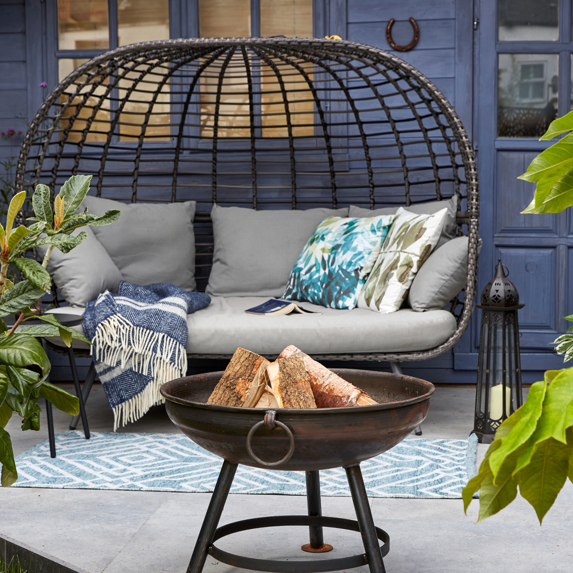 A garden with a curved rattan garden sofa with a firepit and an outdoor floor lamp 