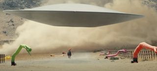 A sleek flying saucer in a desert field with dancing inflatable noodle people.