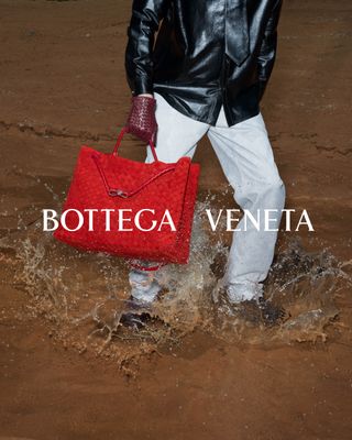 A model in a black leather top, white pants, red gloves, and a red Andiamo bag by Bottega Veneta