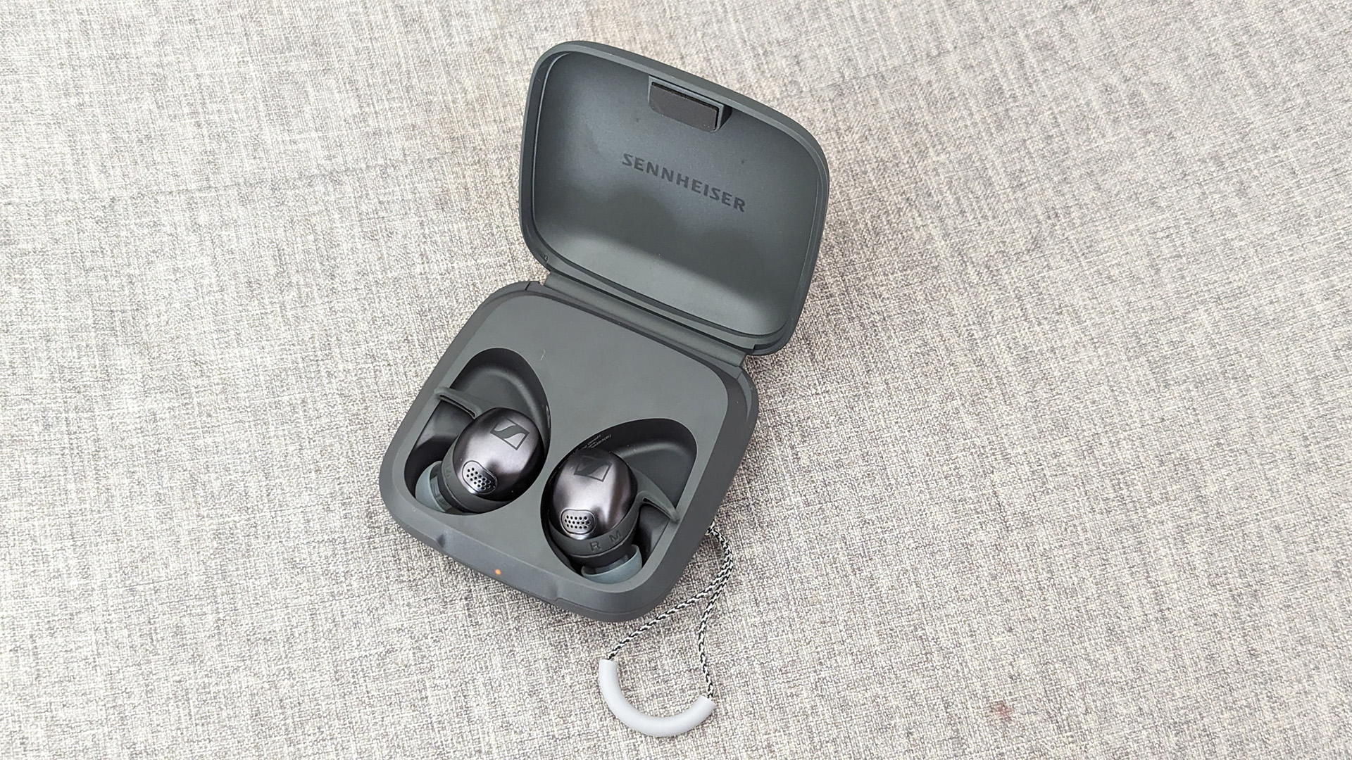 Sennheiser Momentum Sport in-ear headphones in open case on grey fabric background
