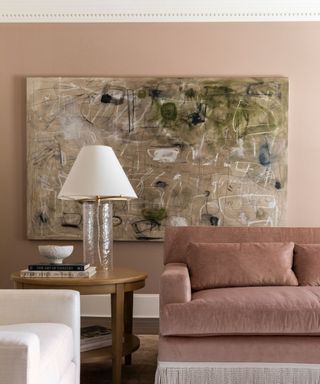 living room with pink wall, pink sofa, abstract canvas artwork and wooden side table with cream lamp