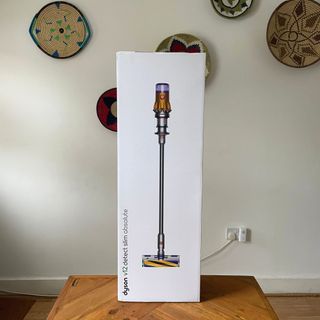 Dyson V12 Detect Slim Absolute box standing on a wooden table in front of a white wall with colourful baskets on it