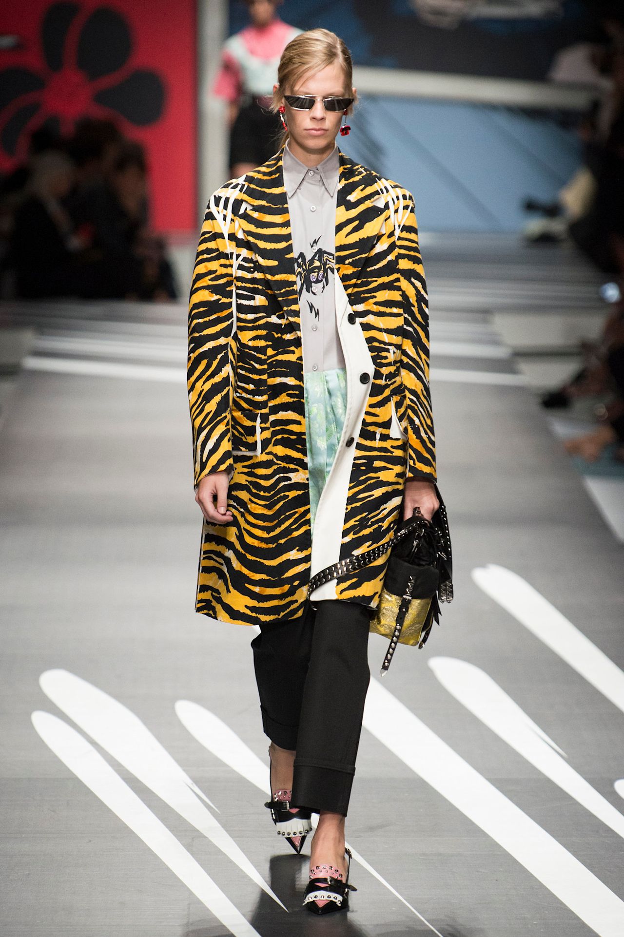 A model wearing an oragnge tiger print jacketwith a white and colorful blouse and blac pants at Prada Spring 2018