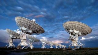 ten large white radio telescopes point up at a cloudy sky.