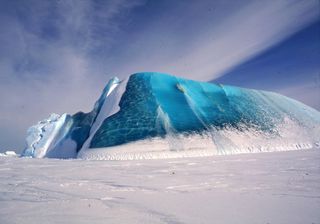 An iceberg near Davis Station, Antarctica, incorporates glacial ice (white) and marine ice (blue). Researchers stand on snow-covered sea ice in this 1996 photo.