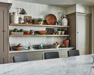 Kitchen cabinets in a muted shade with open shelving above and in between floor to ceiling cabinets