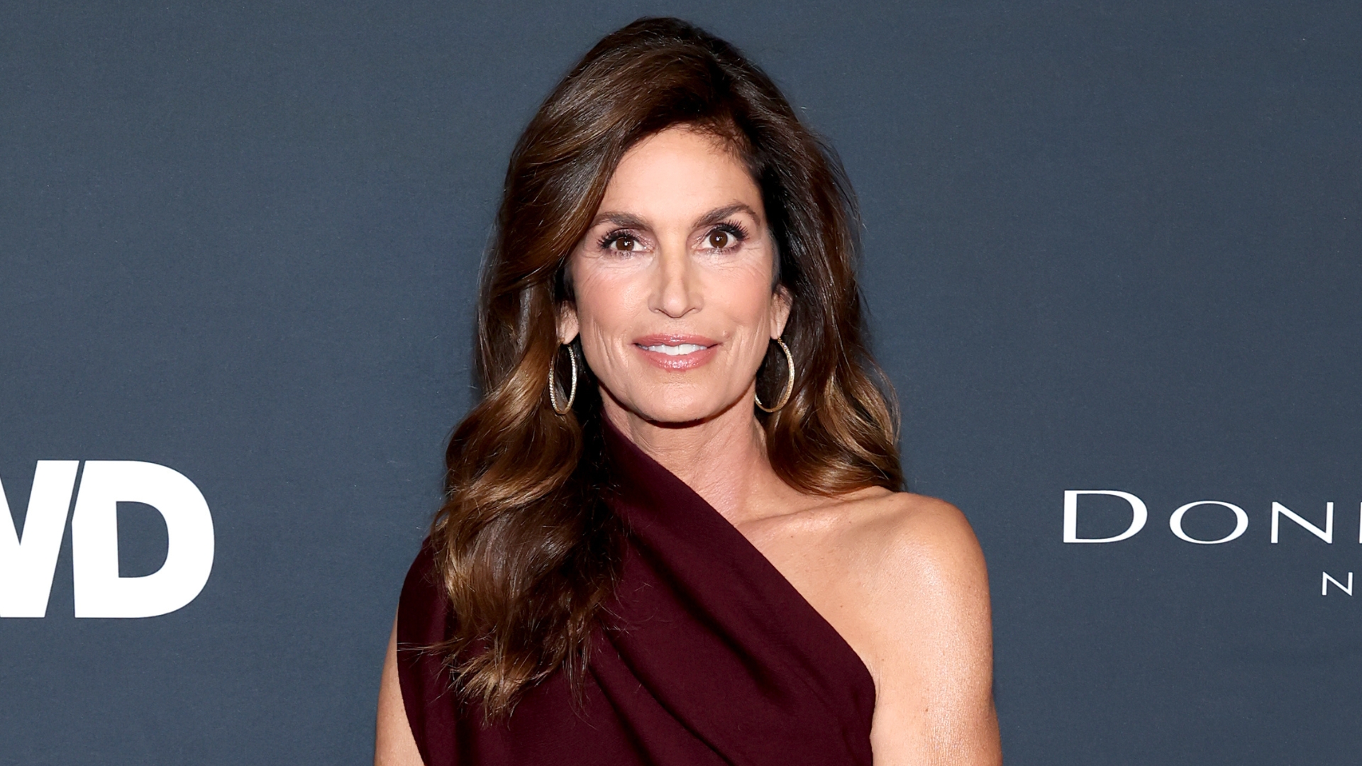 Cindy Crawford is pictured with loosely-curled brunette hair and wearing a one-shoulder brown dress at The 2026 WWD Style Awards presented by Women's Wear Daily at Regent Santa Monica Beach on January 09, 2026, in Santa Monica, California. 