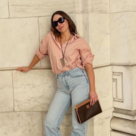 a woman wearing a pink button-down, light-wash straight-leg jeans, and white flats