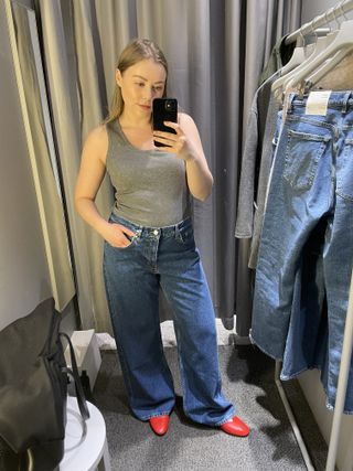 Woman in dressing room wears grey tank top, blue jeans, red shoes