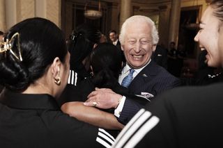 King Charles hugging a group of women wearing black rugby jerseys and laughing