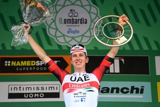 Tadej Pogacar celebrates on the podium of the 2022 Il Lombardia holding up his trophy and flowers