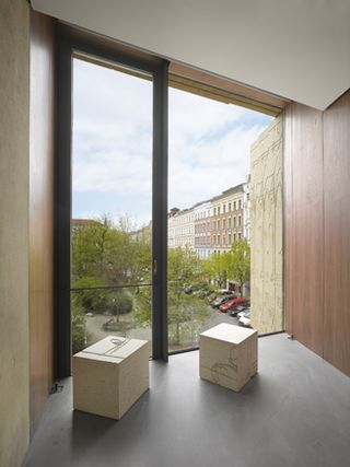 Two blocks (one rectangle and one square) photographed against a floor to ceiling window and grey floor with views of the outside