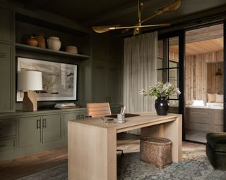 moody home office with dark olive green walls and built-in storage, modern wooden desk and gold ceiling light