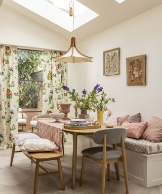 Bright white dining room with wooden dining table, floral curtains, low hanging pendant and floral artwork