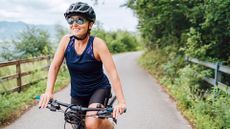 Woman doing cycling as a workout on bike outdoors in the fresh air, wearing helmet, sunglasses and bike shorts