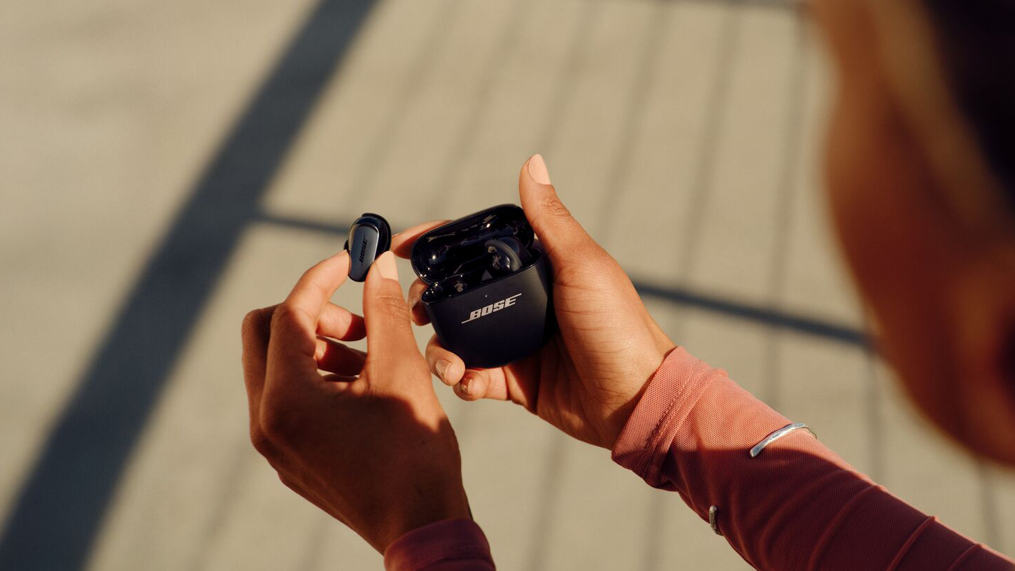 A woman is removing the Bose QuietComfort Ultra Earbuds 2nd Gen from their case while outdoors