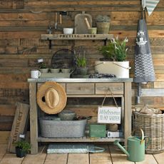 Potting shed filled with a work bench, and garden accessories like a watering can and plants