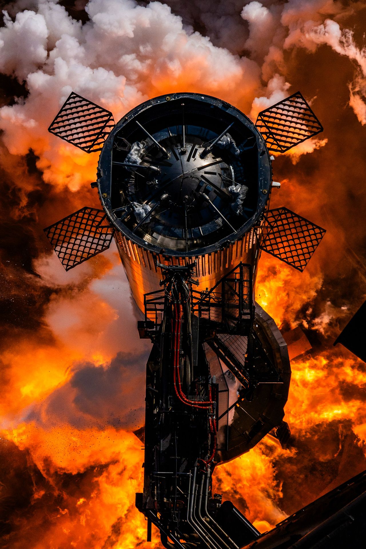 fiery smoke rises from below as a tall chrome cylinder stands next to a tower