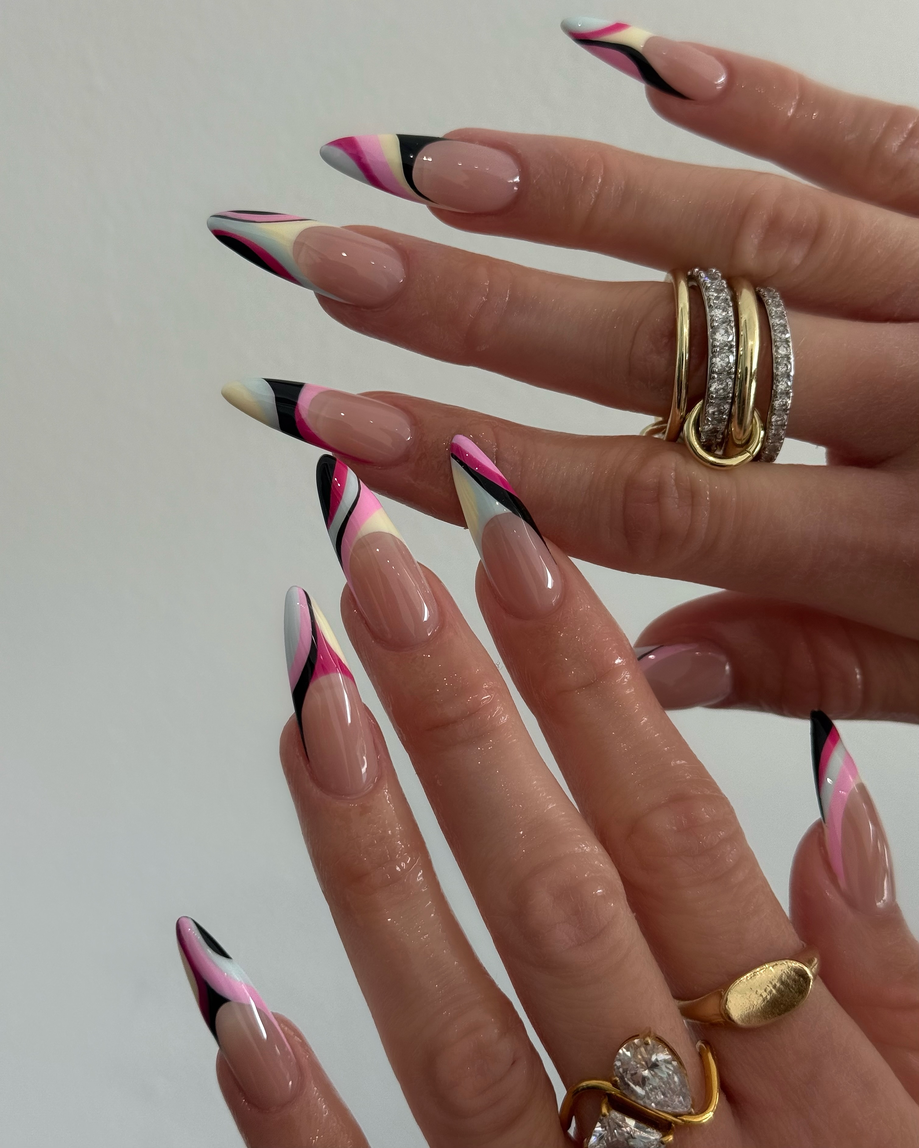 Colorful swirl nail art inspired by a Pucci print with stacks of gold rings
